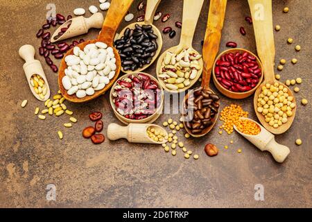 Ensemble de diverses légumineuses sèches en cuillères en bois, protéine indispensable pour un mode de vie sain. Assortiment de différents types de haricots. Cuisson en béton de pierre Banque D'Images