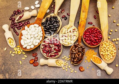 Ensemble de diverses légumineuses sèches en cuillères en bois, protéine indispensable pour un mode de vie sain. Assortiment de différents types de haricots. Cuisson en béton de pierre Banque D'Images
