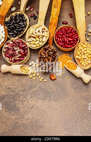 Ensemble de diverses légumineuses sèches en cuillères en bois, protéine indispensable pour un mode de vie sain. Assortiment de différents types de haricots. Cuisson en béton de pierre Banque D'Images