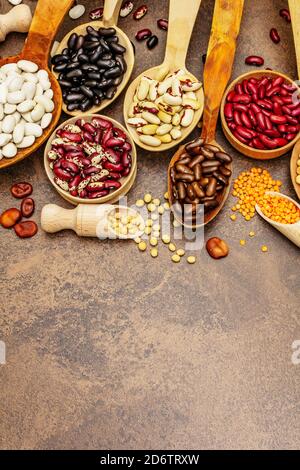 Ensemble de diverses légumineuses sèches en cuillères en bois, protéine indispensable pour un mode de vie sain. Assortiment de différents types de haricots. Cuisson en béton de pierre Banque D'Images