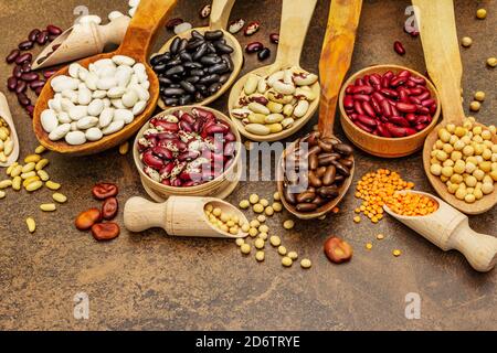 Ensemble de diverses légumineuses sèches en cuillères en bois, protéine indispensable pour un mode de vie sain. Assortiment de différents types de haricots. Cuisson en béton de pierre Banque D'Images