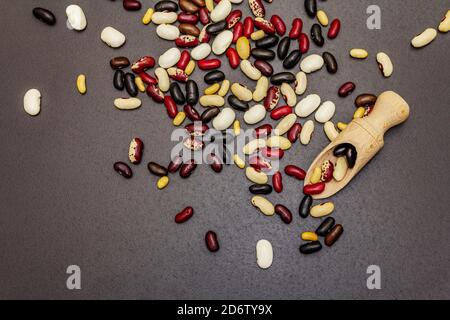 Assortiment de différents types de haricots dans une cuillère en bois. Mélange de différentes légumineuses sèches éparpillées sur fond de béton de pierre noire, vue de dessus Banque D'Images