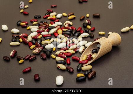 Assortiment de différents types de haricots dans une cuillère en bois. Mélange de diverses légumineuses sèches dispersées sur fond de béton de pierre noire, gros plan Banque D'Images