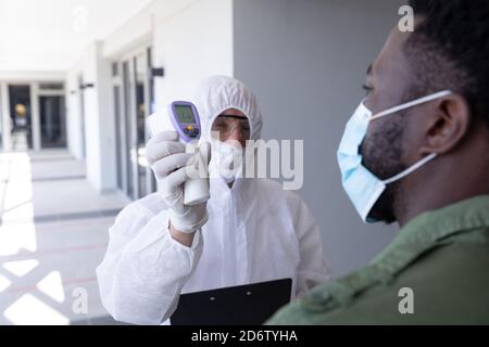 Travailleur de la santé portant des vêtements de protection montrant la température à l'homme d'affaires Banque D'Images