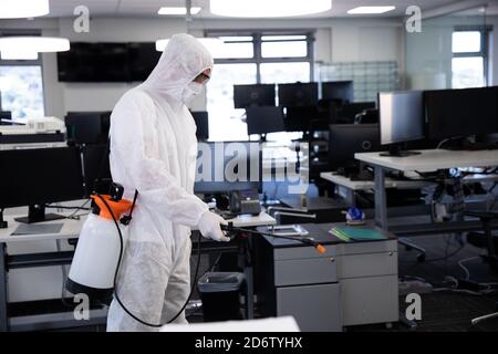 Travailleur portant une combinaison de protection, un masque facial et des gants désinfectant le bureau à l'aide d'un spray désinfectant antibactérien. Hygiène sur le lieu de travail pendant Coronav Banque D'Images