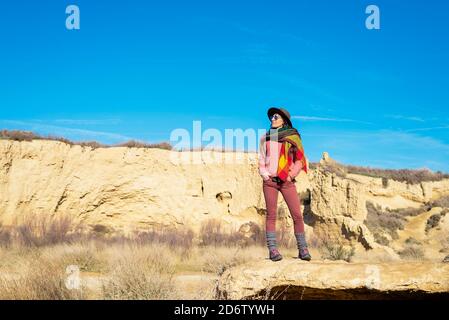 Belle femme avec chapeau et lunettes de soleil debout sur le désert pendant regarder l'appareil photo Banque D'Images