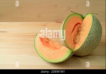 Tranche de melon de musc mûr frais coupée en tranches de fruits entiers isolé sur une table en bois Banque D'Images