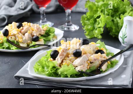 Deux assiettes avec salade d'ananas, poulet cuit au four, maïs et olives noires et deux verres de vin rouge Banque D'Images