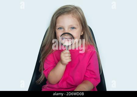 Blonde blanche fille utilise une loupe sur elle ouverture de la bouche souriant à la caméra sur un mur blanc de studio Banque D'Images