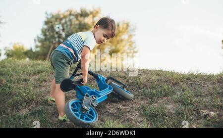 Un garçon caucasien portant son vélo sur une colline tout en jouant dans un champ vert Banque D'Images