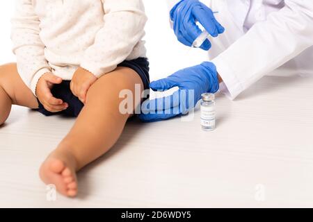 Vue rognée de la seringue de maintien du pédiatre près du vaccin et de l'enfant en bas âge garçon isolé sur blanc