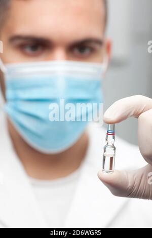 Gros plan du médecin avec masque chirurgical tenant une ampoule avec vaccin dans sa main - se concentrer sur l'ampoule Banque D'Images