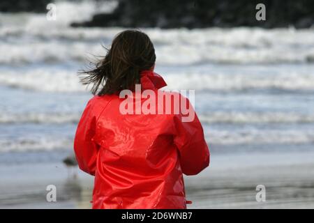 Ayr, Ayrshire, Écosse, Royaume-Uni : femme blanche et attrayante de race blanche dans ses 20 ans qui a acheté un imperméable PVC de seconde main le porte sur une journée venteuse sur la plage. Col relevé par temps froid et vent Banque D'Images