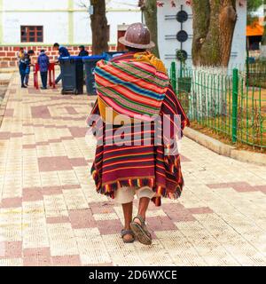 Homme indigène bolivien de Tarabuco en vêtements traditionnels (poncho et chapeau) marchant sur la place principale, Tarabuco, Bolivie. Banque D'Images