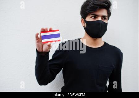 Homme asiatique porter tout noir avec masque de visage tenir drapeau de Thaïlande à la main isolé sur fond blanc. Concept de pays du coronavirus. Banque D'Images