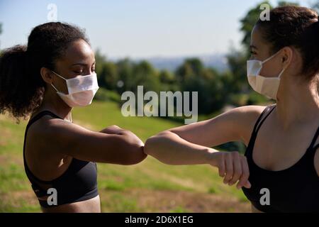 Tenue africaine et indienne sport dames amis porter masque visage donner le choc de coude. Banque D'Images