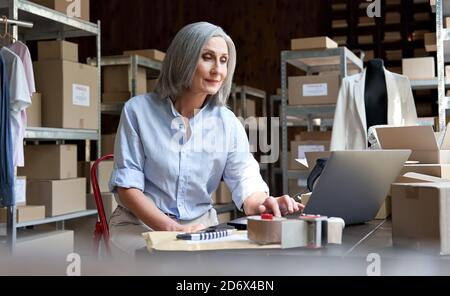 Femme mature vendeur utilisant la vérification par ordinateur ecommerce vêtements commandes. Banque D'Images