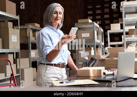 Une femme propriétaire de petite entreprise utilisant une application mobile sur son smartphone pour vérifier la boîte à colis. Banque D'Images