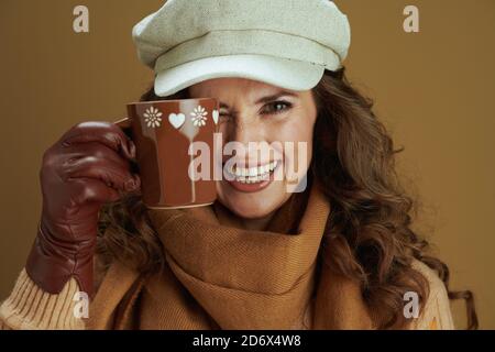 Bonjour octobre. Portrait d'une femme au foyer souriante et tendance dans un foulard avec des gants en cuir et une tasse isolée sur fond beige. Banque D'Images