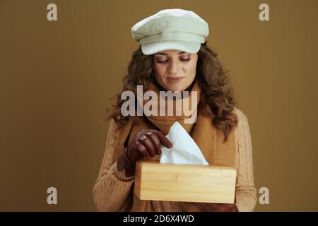 Bonjour novembre. Femme au foyer tendance de 40 ans en foulard avec mouchoirs en papier et gants en cuir sur fond beige. Banque D'Images