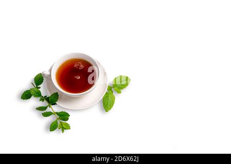 Une tasse de thé noir sur une soucoupe avec des feuilles de menthe sur un fond blanc isolé. Espace pour la copie. Banque D'Images