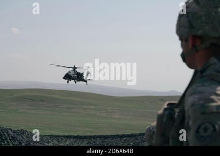 Un hélicoptère Apache AH-64 américain vole par un soldat américain, affecté au 4e Escadron, 2e Régiment de cavalerie, lors d'un appel à l'entraînement d'incendie avec la 12e Brigade de l'aviation de combat à la zone d'entraînement de Vaziani, Géorgie, le 14 septembre 2020. Les 4/2 soldats ont terminé avec succès leur entraînement dans la zone d'entraînement de Vaziani en Géorgie du 7 au 18 septembre. Conçu pour améliorer les partenariats régionaux et accroître l'état de préparation et l'interopérabilité de la force américaine, l'exercice permet aux participants d'effectuer des gammes de sniper et de démonstration, des exercices d'entraînement situationnel, des exercices de tir en direct et des exercices de c Banque D'Images