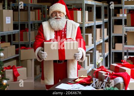 Joyeux Père Noël portant un costume tenant une boîte cadeau dans un atelier, portrait. Banque D'Images