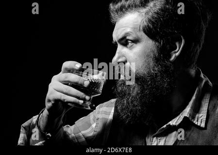 Un élégant homme souffrant d'alcoolisme de boire du whisky. Beau homme barbu tenant un verre de whisky. Un homme séduisant dans la barre à whisky. Banque D'Images