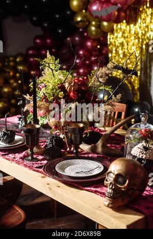 Vider la belle table servie pour halloween. Plaques sur la table à côté des crânes, araignées et branches sur un fond de boules violettes. Banque D'Images