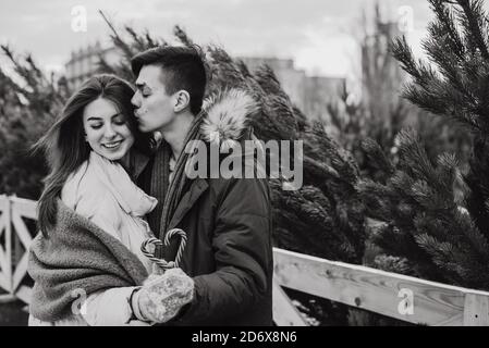 Un jeune couple tient une canne en sucre en forme de coeur et enserre. Portrait urbain des amoureux. Concept Noël, nouvel an et amour. Extérieur. Banque D'Images