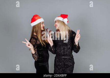 Deux jeunes femmes adorables en robes noires et chapeaux de père noël ayant du plaisir et célébrant une fête de Noël dans le studio. Banque D'Images