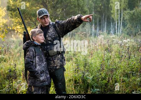 Fête des pères. Père avec un fusil montrant quelque chose à son fils tout en chassant sur une nature. Bonne famille, fête des Pères et vacances d'été locales Banque D'Images