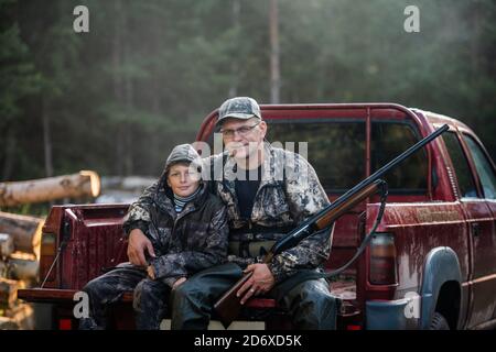 Père dans un chapeau et son fils assis dans une voiture après la chasse. Banque D'Images