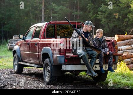 Père dans un chapeau et son fils assis dans une voiture après la chasse. Banque D'Images