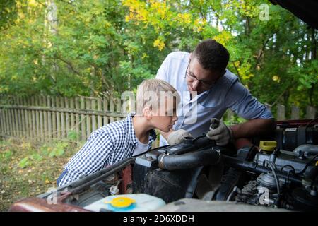 Papa et son fils réparent la voiture avec le capot ouvert à l'extérieur, fixant le moteur Banque D'Images