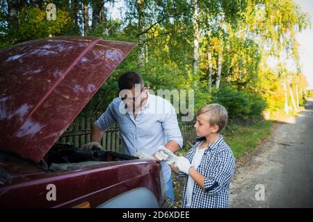 Papa et son fils réparent la voiture avec le capot ouvert à l'extérieur, fixant le moteur Banque D'Images