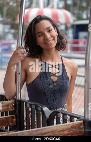 jeune femme latine gaie avec de courts cheveux ondulés souriant et debout dans un parc portant un chemisier noir Banque D'Images