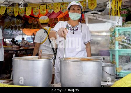 Nouvelle normale. Le célèbre sourire thaïlandais caché derrière un masque facial. Une femme thaïlandaise heureuse et souriante dans sa stalle du marché. Thaïlande S. E. Asie. Banque D'Images