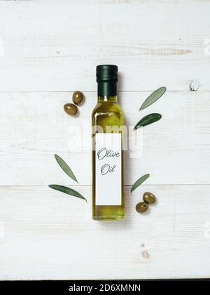 Maquette de bouteille en verre à l'huile d'olive. Vue de dessus d'une bouteille en verre vert avec de l'huile d'olive extra vierge sur fond de bois blanc avec des olives vertes et des feuilles d'oliviers verts frais. Verticale. Copier l'espace. Banque D'Images