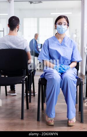 Un assistant épuisé dans la salle d'attente de l'hôpital pendant une pandémie mondiale de coronavirus. Médecin consultant l'homme senior dans la salle d'examen. Médecin, épidémie, soins, chirurgie, couloir. Banque D'Images