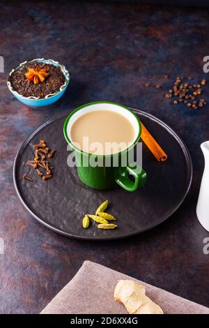 Thé Chai de masala. Boisson traditionnelle indienne - thé masala avec diverses épices sur une assiette noire. Tasse d'épices en céramique, thé et pot à lait