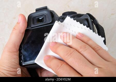 Les mains wipind l'écran d'un appareil photo reflex numérique avec un chiffon en microfibre. Élimination régulière de la poussière et des traces de doigts de l'équipement photographique. Gros plan sur l'entretien Banque D'Images