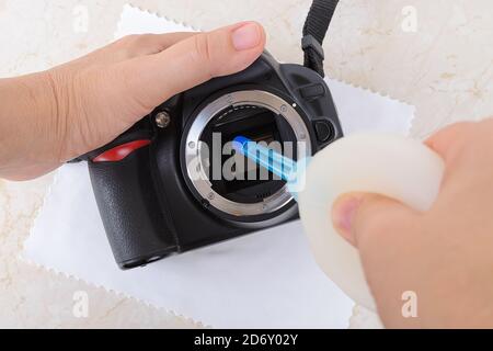 Mains soufflant la poussière du miroir de l'appareil photo reflex numérique à l'aide d'un souffleur d'air en silicone. Élimination régulière de la poussière et des taches des équipements photographiques. Entretien. Banque D'Images