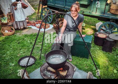 Cuisine de style rétro dans la nature. Femme assise près du feu où la nourriture est cuite. Banque D'Images