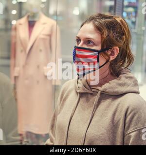 Femme dans un masque médical se tient près de mannequins avec des vêtements. Jeune femme dans un masque avec un drapeau américain, mode de vie portrait Banque D'Images