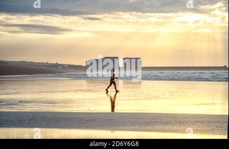 Brighton, Royaume-Uni, le 20 octobre 2020 - UN nageur traverse la plage à marée basse à Brighton tôt aujourd'hui, le matin d'une matinée pleine de brise mais de lumière. Des conditions humides et venteuses sont prévues pour les prochains jours dans toute la Grande-Bretagne comme Storm Barbara approche de l'Europe : crédit Simon Dack / Alamy Live News Banque D'Images