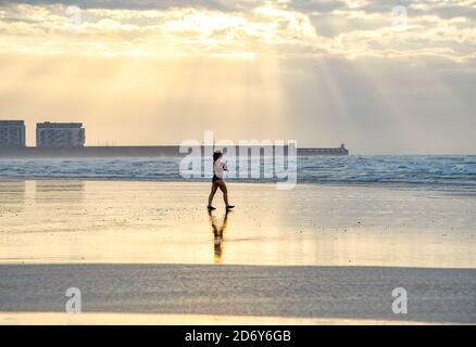 Brighton, Royaume-Uni, le 20 octobre 2020 - UN nageur traverse la plage à marée basse à Brighton tôt aujourd'hui, le matin d'une matinée pleine de brise mais de lumière. Des conditions humides et venteuses sont prévues pour les prochains jours dans toute la Grande-Bretagne comme Storm Barbara approche de l'Europe : crédit Simon Dack / Alamy Live News Banque D'Images