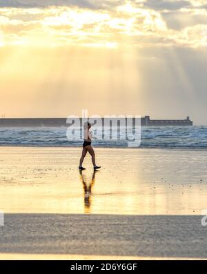 Brighton, Royaume-Uni, le 20 octobre 2020 - UN nageur traverse la plage à marée basse à Brighton tôt aujourd'hui, le matin d'une matinée pleine de brise mais de lumière. Des conditions humides et venteuses sont prévues pour les prochains jours dans toute la Grande-Bretagne comme Storm Barbara approche de l'Europe : crédit Simon Dack / Alamy Live News Banque D'Images