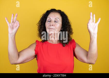 Femme d'âge moyen portant une chemise décontractée sur un jaune isolé arrière-plan se détendre et sourire avec les yeux fermés faisant le geste de méditation avec le doigt Banque D'Images