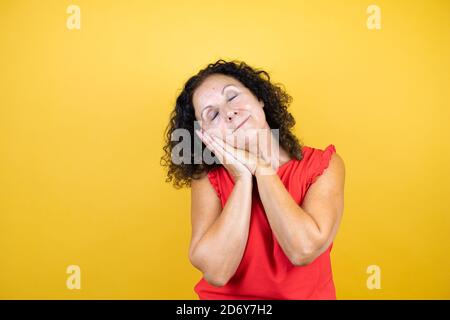 Femme d'âge moyen portant une chemise décontractée sur un jaune isolé arrière-plan dormant fatigué rêvant et posant avec les mains ensemble pendant un accès wi souriant Banque D'Images
